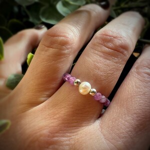 May include: A ring made of small purple beads with a single white pearl in the center.