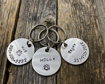 May include: Three silver dog tags with engraved names and phone numbers. The tags are attached to key rings. The names are Max, Molly, and Tiger.