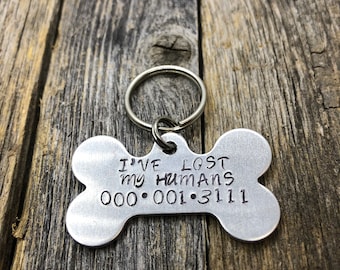 May include: Silver bone-shaped dog tag with a key ring. The tag reads "I've lost my humans 000-001-3111".