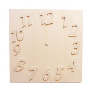 Peut inclure: Un cadran d'horloge carré en bois non fini avec des chiffres en relief de couleur claire de 1 à 12. Un petit trou est centré pour les aiguilles de l'horloge. Le grain du bois est visible, et les chiffres sont légèrement inclinés.