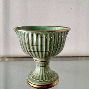 以下が含まれることがあります： ミントグリーンの色合いに茶色の縦縞模様が入った、ヴィンテージスタイルの台座付きボウル。縁と底には金色のトリムが施されています。ボウルは台座に溝のデザインがあり、幅広で開いた上部を備えています。