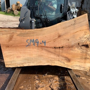 Puede incluir: Una gran losa de madera marr&oacute;n claro con un borde natural y un patr&oacute;n de veta &uacute;nico. La losa est&aacute; marcada con el texto "SM9-4" en tinta azul.