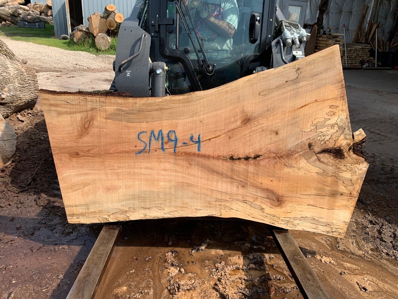 Puede incluir: Una gran losa de madera marr&oacute;n claro con un borde natural y un patr&oacute;n de veta &uacute;nico. La losa est&aacute; marcada con el texto "SM9-4" en tinta azul.