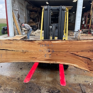 K&ouml;nnte beinhalten: Ein gro&szlig;es, gebogenes St&uuml;ck Holz mit nat&uuml;rlicher Oberfl&auml;che. Das Holz hat einen Riss, der durch die Mitte verl&auml;uft, und ist mit den Zahlen 33, 44 und dem Text "HCK63 < 14B > 3"1" gekennzeichnet. Das Holz wird von einem Gabelstapler angehoben.