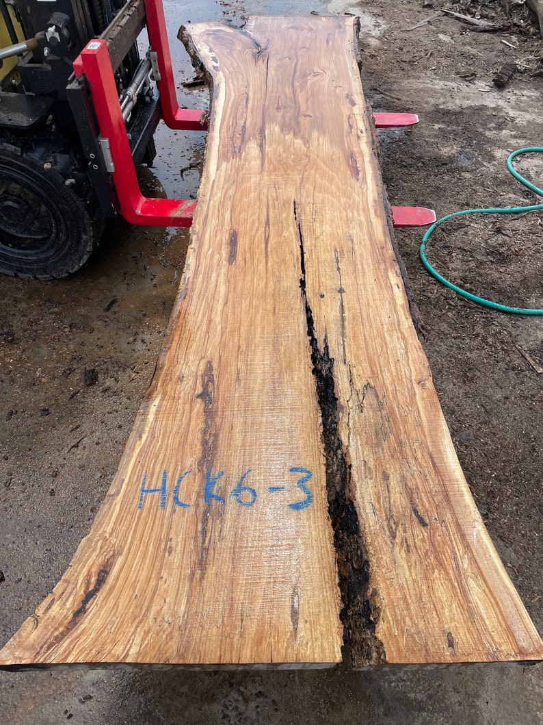 K&ouml;nnte beinhalten: Eine gro&szlig;e, hellbraune Holzplatte mit einer nat&uuml;rlichen Kante. Die Platte hat einen dunkelbraunen Riss, der durch die Mitte verl&auml;uft. Die Platte ist mit blauer Schrift gekennzeichnet, die "HCK6-3" lautet.