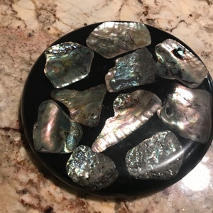 May include: A round black coaster with iridescent shell pieces embedded in the surface.
