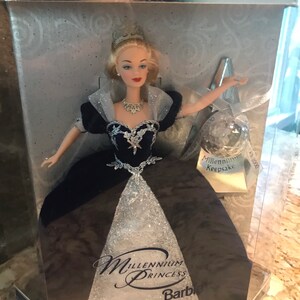May include: A Barbie doll dressed in a silver and black gown with a tiara and necklace. The doll is in a clear plastic box with a silver and blue background. The box says "Special Millennium Edition" and "Millennium Princess Barbie".