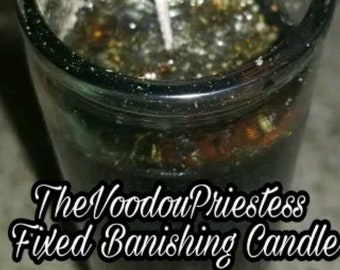 May include: A black glass candle with a white wick and a dark brown wax base. The candle is labeled "The Voodoo Priestess Fixed Banishing Candle".