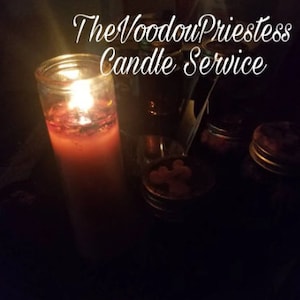 May include: A lit red candle in a glass jar with a label that reads "The Voodoo Priestess Candle Service". There are three smaller jars with lids on a dark surface.