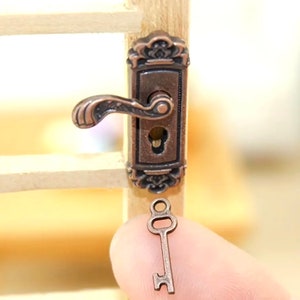 May include: A miniature door handle with a keyhole and a decorative design. The handle is made of metal and has a bronze finish. A small key with a bronze finish is shown in the image.