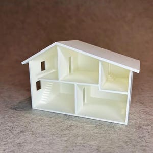May include: A white, open-faced dollhouse model featuring a gabled roof, multiple interior rooms, and staircases. The structure is divided into two levels with several rectangular openings serving as doorways and windows throughout the interior.