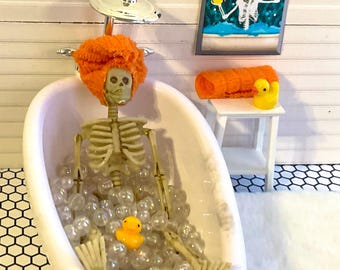 Casa de muñecas en miniatura con esqueleto en baño de burbujas, alfombra blanca peluda, mesa de madera blanca, imagen de esqueleto en baño o toalla naranja y pato. 1:12