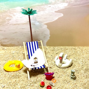 May include: A miniature beach scene with a blue and white striped beach chair, a yellow inflatable ring, a white swan inflatable ring, a red bucket, a small palm tree, and a bottle of sunscreen.