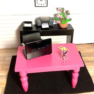 May include: A pink desk with a black laptop, a glass jar with pencils, and a black and white clock on the wall behind it.