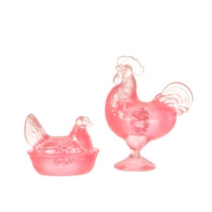 May include: A set of two pink glass rooster and hen figurines. The rooster is standing on a base and the hen is sitting in a nest.