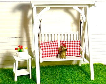 May include: White wooden swing set with a red and white checkered cushion. A small white stool with a swan figurine is in the foreground.