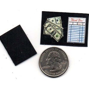 May include: A miniature black tray with a stack of dollar bills and a miniature receipt that says "Thank You!" on a white background.