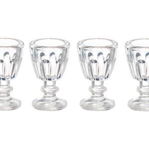May include: Four clear, stemmed shot glasses with a cut-glass design. The glasses have a rounded bowl, a short stem, and a circular base. The glasses are arranged in a row against a white background.