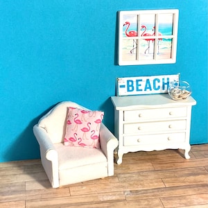 May include: White armchair with a pink flamingo patterned pillow, a white dresser with three drawers, a sign that says "BEACH", and a framed picture of pink flamingos on a beach.