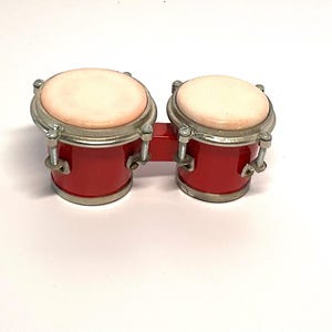 May include: A pair of red conga drums with white drumheads and silver hardware. The drums are connected by a metal bar.