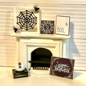 May include: A white miniature fireplace mantel decorated for Halloween with a black spiderweb, a black spider, a white pumpkin with a black spider, a sign that says "BOO." and a sign that says "HAPPY HALLOWEEN".