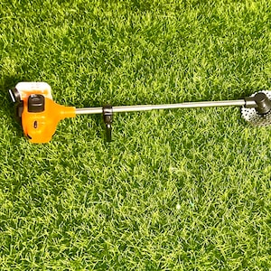 May include: An orange and black electric string trimmer with a silver shaft and a round cutting head. The trimmer is on a green artificial grass surface.