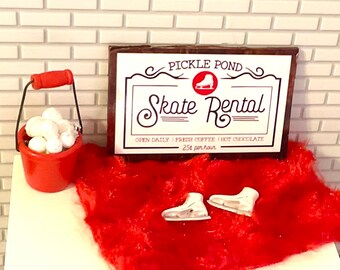 May include: A wooden sign with the text "Pickle Pond Skate Rental" in white lettering on a brown background. The sign also includes the text "Open Daily | Fresh Coffee | Hot Chocolate | 2.50 per hour". There are white ice skates on a red fuzzy surface.