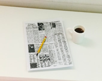 May include: A white coffee mug with a black liquid inside, a yellow pencil, and a newspaper with the text "A Singer's Intimate Story" and "A Girl and Her Goldfish".