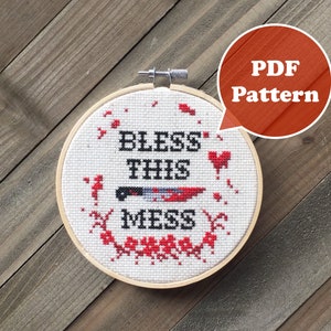May include: A white embroidery hoop with a cross-stitch design that says "Bless This Mess" with a bloody knife and red hearts. The hoop is on a wooden background. PDF Pattern.