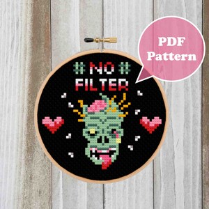 May include: Cross stitch pattern featuring a zombie with the text "#NO# FILTER" in a black hoop. The zombie is green with a pink brain and has a red tongue sticking out. There are two pink hearts on either side of the zombie.