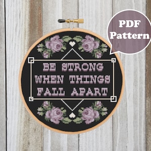 May include: A black and white cross-stitch pattern with the text "BE STRONG WHEN THINGS FALL APART" surrounded by purple flowers. The pattern is in a wooden embroidery hoop and labeled "PDF Pattern".