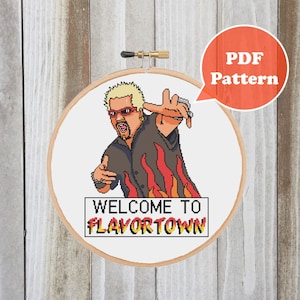 May include: Cross stitch pattern featuring a cartoon illustration of a man with a blonde mohawk, sunglasses, and a black shirt with flames. The text "Welcome to Flavortown" is below the illustration. The pattern is available as a PDF download.
