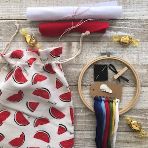 Puede incluir: Una bolsa de tela con estampado de sand&iacute;a con cierre de cord&oacute;n, un aro de bordado de madera con hilo, una aguja y un trozo de tela. El aro de bordado tiene un di&aacute;metro de 25 cm.