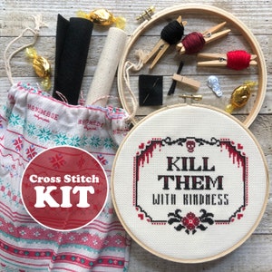 May include: Cross stitch kit with a red and white fabric bag, a wooden embroidery hoop, red and black embroidery floss, a needle, and a piece of black felt. The embroidery hoop has white Aida cloth with a red and black cross stitch design that says "Kill them with kindness".