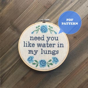 Peut inclure: Un cerceau de broderie blanc avec un motif floral bleu et le texte "need you like water in my lungs". Le cerceau est sur une surface en bois. Modèle PDF inclus.