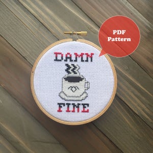 Peut inclure: Un cerceau de broderie en point de croix blanc avec un motif rouge et noir qui dit "DAMN FINE" avec une tasse de café au milieu. Le cerceau est sur une surface en bois.
