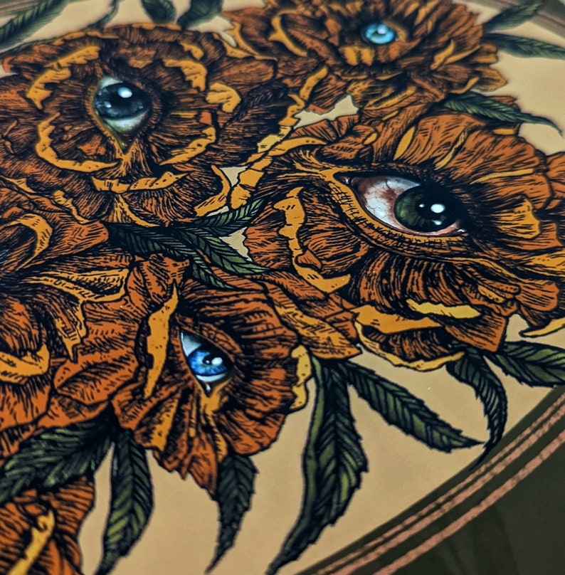 Photo of an art print showing hand drawn golden flowers with photorealistic eyes at the centre of each.