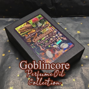 May include: A black box with a label that reads "Andromeda's Curse Goblincore Perfume Oil Collection". The label features a toad, a mushroom, and other nature-inspired elements. The box is sitting on a black and gold patterned surface.
