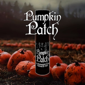 Może przedstawiać: Czarna cylindryczna butelka olejku perfumowanego z etykietą zawierającą tekst Pumpkin Patch oraz Andromeda's Curse Perfume Oil - 10ml. Projekt etykiety zawiera grafikę białych gwiazd i wiszących świateł na ciemnym tle.