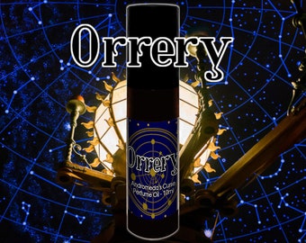 May include: A dark brown glass bottle with a black cap and a blue and gold label. The label reads "Orrey Andromeda's Curse Perfume Oil - 10ml". The bottle is in front of a dark blue background with white stars.