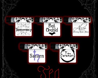 Puede incluir: Cinco viales de vidrio transparente con tapas negras, cada uno con una etiqueta blanca con texto y gráficos en negro. Las etiquetas incluyen Tasseomancy, Bat Orchid, Alice Moving Under Skies, Saturn con un símbolo morado y Tea Ceremony.