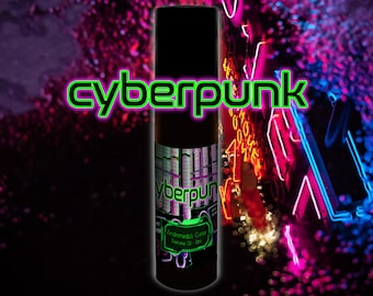 May include: A cylindrical black perfume oil bottle with a label featuring the text 'cyberpunk' in bright green, along with 'Andromedas Curse' and 'Perfume Oil - 10ml'. The bottle is centered against a dark, blurred background with neon pink and blue lights.