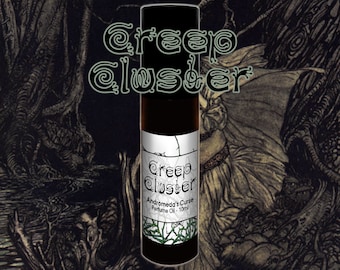 May include: A black roll-on bottle with a white label that reads "Creep Cluster Andromeda's Curse Perfume Oil - 10ml". The bottle is in front of a dark, illustrated background.
