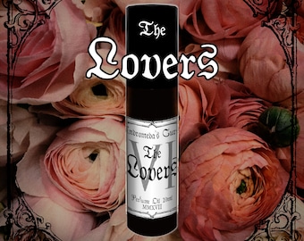 May include: A black roll-on bottle of perfume oil labeled "Andromeda's Cur The Lovers Perfume Oil 10ml MMXVII". The bottle is surrounded by pink flowers.