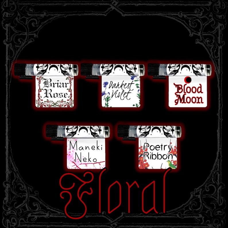 May include: Five small perfume bottles with labels reading "Briar Rose," "Darkest Violet," "Blood Moon," "Maneki Neko," and "Poetry Ribbon." The word "Floral" is written in red script at the bottom. The background is black.
