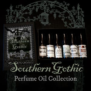 May include: A collection of six small glass perfume oil bottles housed in a black box. The labels feature text including Swamp Witch, Suwannee, Black Phillip, Scrying Orb, and Blood Moon. The box lid displays the text Andromeda's Curse Southern Gothic.