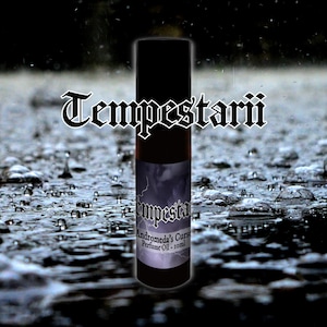 May include: A cylindrical perfume oil bottle with a black cap and a label featuring a lightning storm graphic. The label text reads Tempestarii, Andromeda's Curse, and Perfume Oil - 10ml. The bottle is centred against a dark, rainy background.