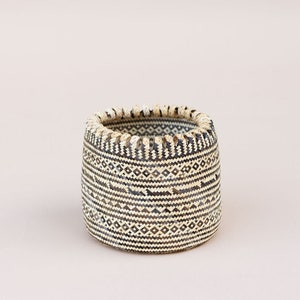 May include: A woven basket with a black and white geometric pattern. The basket is cylindrical and has a slightly flared rim.