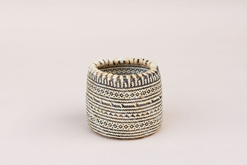 May include: A woven basket with a black and white geometric pattern. The basket is cylindrical and has a slightly flared rim.