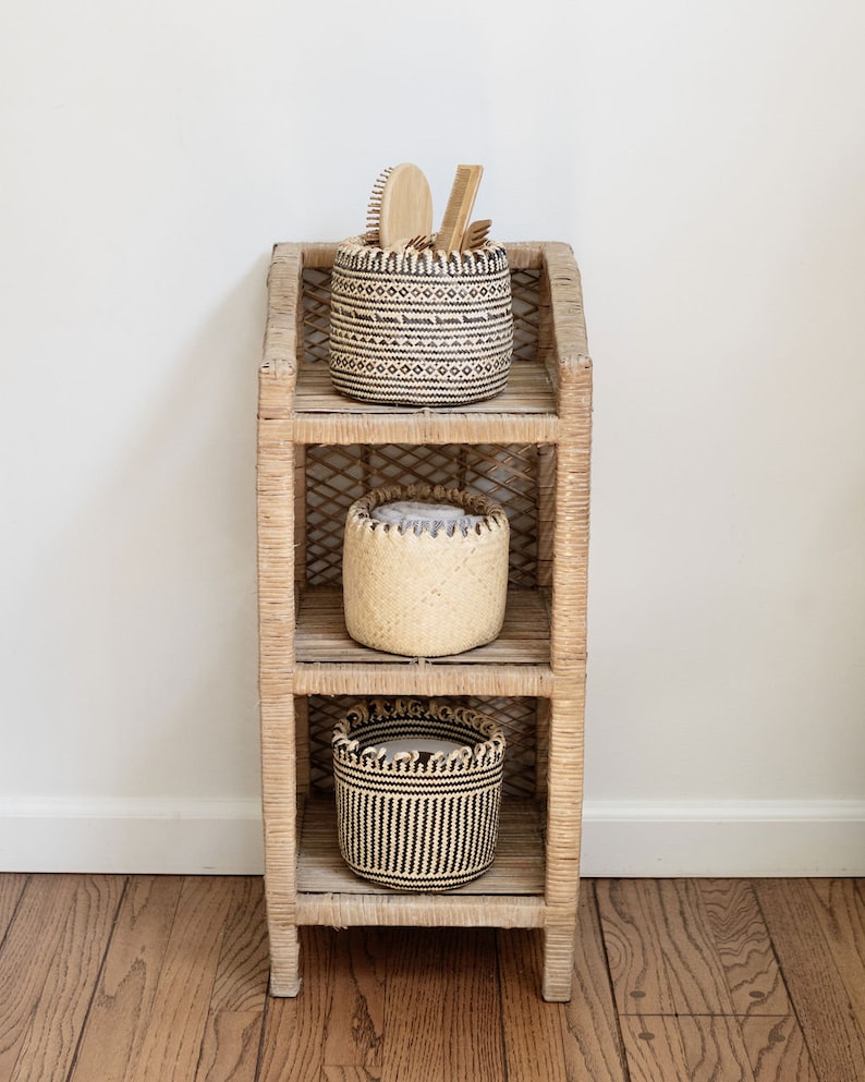 May include: A three-tiered wicker shelf unit with three woven baskets. The top basket is black and white with a geometric pattern and contains wooden brushes. The middle basket is natural woven and the bottom basket is black and white with a striped pattern.